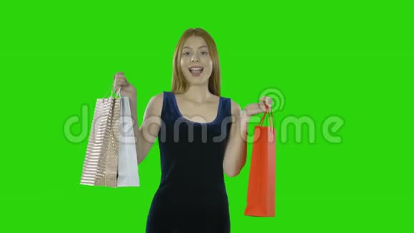 一幅幸福的女孩穿着一件连衣裙手里拿着购物袋的肖像在一个孤立的绿色屏幕上微笑着视频的预览图