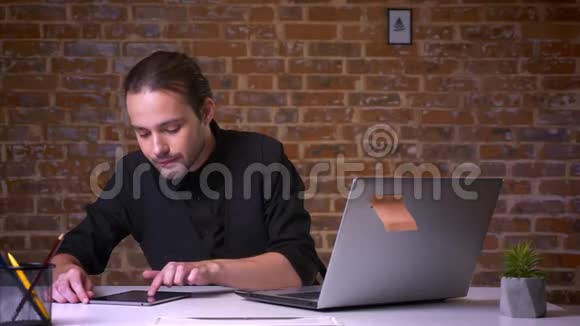 漂亮的白种人成年男子一边看着电脑一边穿着黑色西装坐在办公室里视频的预览图