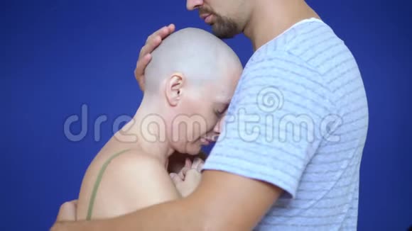 男人在蓝色背景上拥抱一个悲伤的秃头女人肿瘤学的概念和化疗的效果视频的预览图