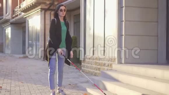 年轻的盲人带着一个带拐杖的背包穿过城市的日光浴视频的预览图