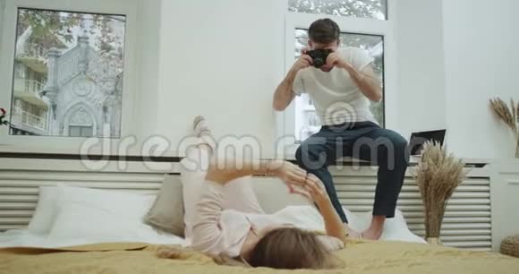 年轻女士穿着睡衣在现代床上为男朋友摆姿势拍照气氛非常美丽视频的预览图