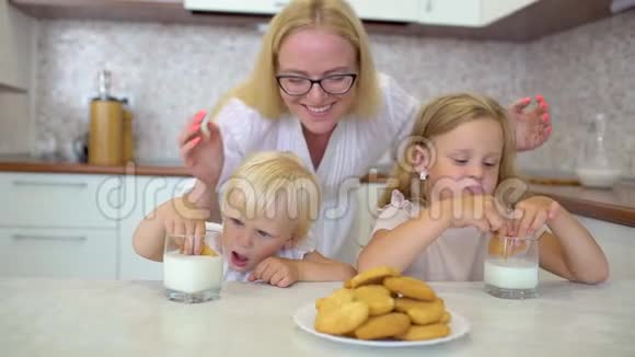 家庭幸福有金发的小女孩在厨房里和妈妈一起吃牛奶和饼干儿童视频的预览图