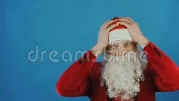 圣诞节和2019年新年像圣诞老人一样的人惊讶地双手抱着他的头蓝色的背景视频的预览图
