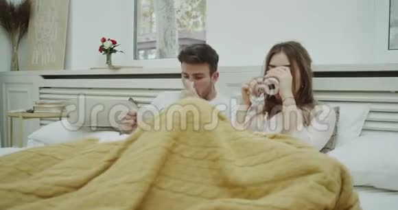 一对穿着睡衣躺在床上的夫妇患了流感咳嗽感觉一点也不好喝了一些温暖的东西视频的预览图