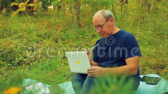 一个戴眼镜的人手里拿着一支铅笔手里拿着一台笔记本电脑在森林视频的预览图