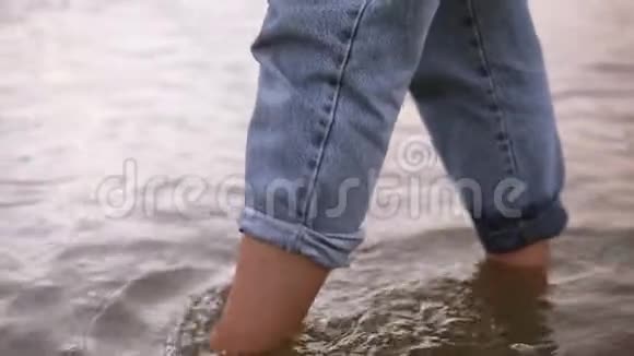 特写一个年轻女人的脚在水中行走镜头湖里穿着蓝色牛仔裤白天夏天视频的预览图
