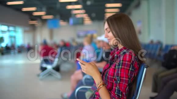 一个女人坐在国际机场的候机楼里等待她的航班使用智能手机城市机场视频的预览图