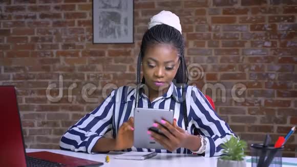可爱的非洲女性带着微笑的脸展示着绿色的屏幕坐在有砖背景的办公桌前视频的预览图