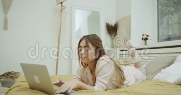漂亮的女士在她舒适的床上看着和敲击她的笔记本视频的预览图