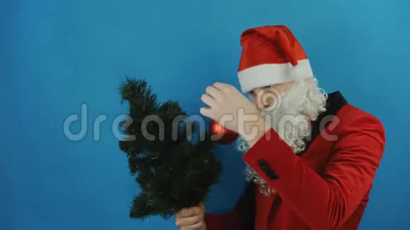 2019年像圣诞老人一样的人在蓝色背景下观看圣诞树和红球玩具视频的预览图