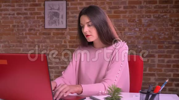 可爱的白种人女性坐在工作场所在工作室里轻松地用笔记本电脑打字视频的预览图