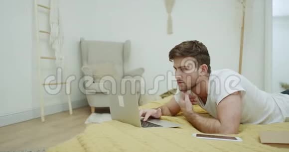 穿着睡衣的人躺在床上在他的笔记本上工作现代卧室视频的预览图