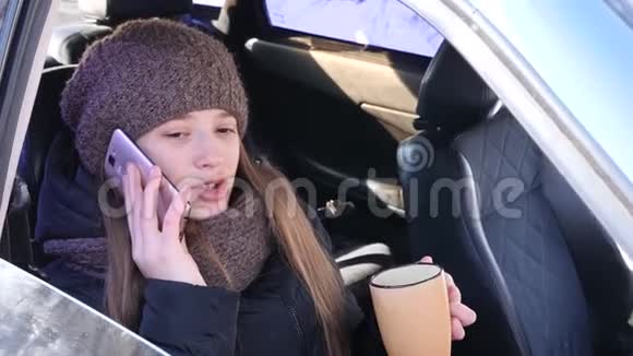 年轻漂亮的女孩坐在车前座位上打电话喝咖啡微笑视频的预览图