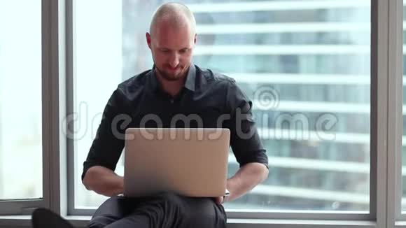 年轻的商人正拿着笔记本电脑坐在办公室的地板上视频的预览图