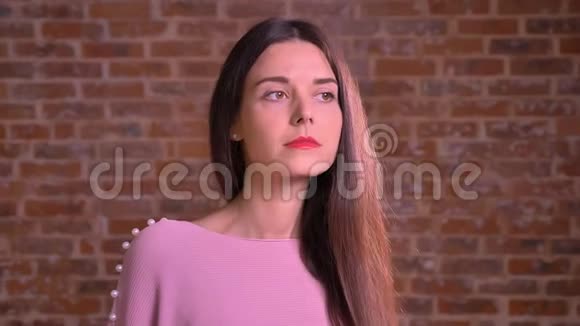 穿着粉红色套头衫的白种人漂亮女孩站在砖墙旁边神情严肃视频的预览图