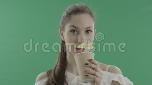 年轻女子在绿色背景下用吸管喝鸡尾酒视频的预览图