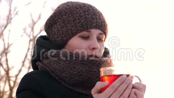 年轻的女孩在寒冷的冬天用热茶温暖自己微笑着视频的预览图