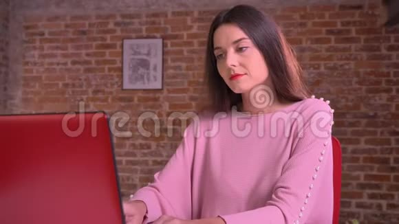 漂亮的高加索女人在她的红色笔记本电脑上打字看着镜头脸上带着幸福的笑容视频的预览图