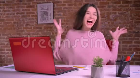 积极的白种人女性在室内工作时在书桌笔记本电脑前开心地笑着握手视频的预览图
