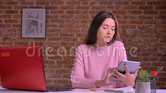 可爱的白种人女性在餐桌上的红色工作室里展示着绿色的屏幕严肃的集中着脸视频的预览图