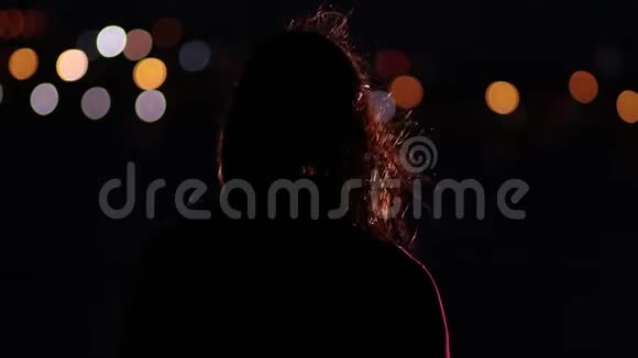 体贴的女人站在夜晚的风中对抗夜晚的城市灯光视频的预览图