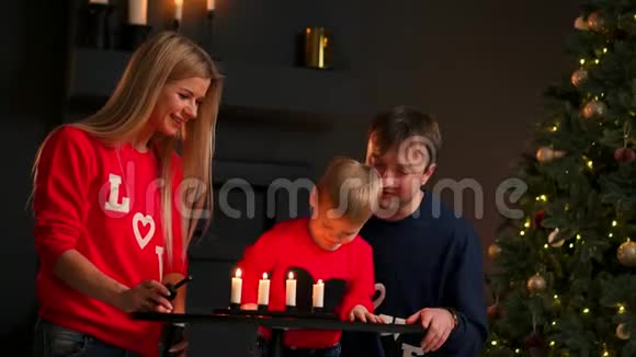 一家人在圣诞节坐在树下看着孩子吹灭蜡烛笑妈妈爸爸笑着视频的预览图