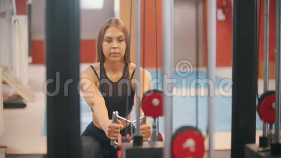 一位在健身房训练的女运动员把手柄拉到重量块上视频的预览图