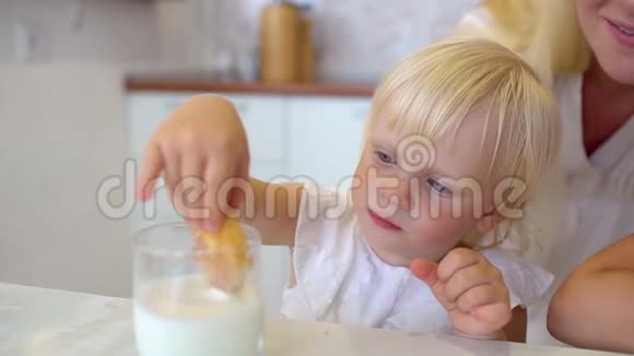 一个金发可爱的小女孩坐在家里的厨房里吃饼干的画像视频的预览图