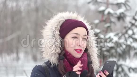 在冬天的公园里散步时美丽的年轻女孩正积极地翻阅着智能手机上的新闻视频的预览图