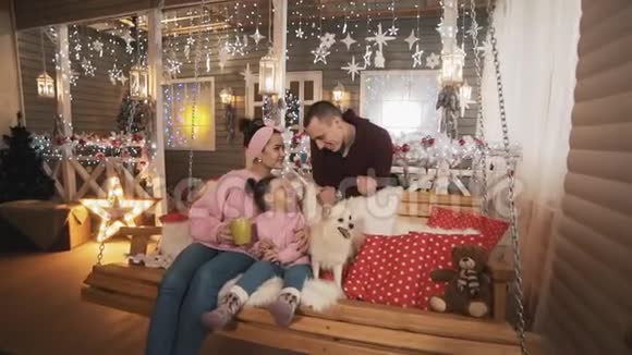 一家人带着女儿和白狗在门廊的圣诞长椅上玩得很开心视频的预览图