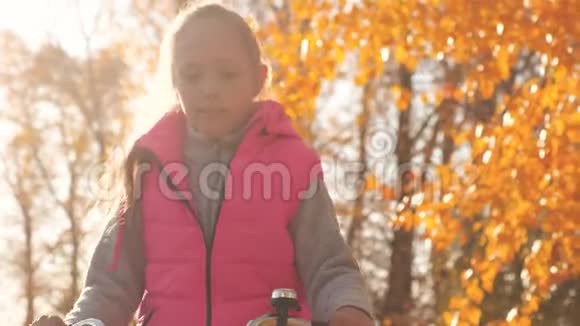 穿粉红色夹克的女孩在秋天的公园里骑自行车背景是黄树视频的预览图