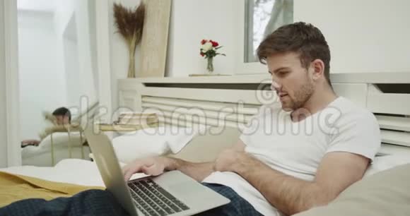有魅力的年轻人透过笔记本电脑在舒适的床上工作4k拍摄红色史诗视频的预览图