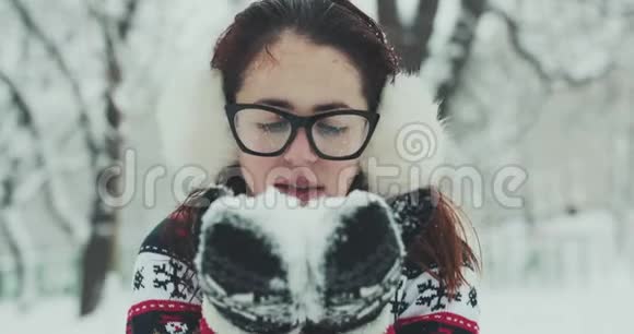 年轻的女人把白色的雪花吹进相机快乐的女孩在冬天送雪吻嬉戏的女人吹视频的预览图