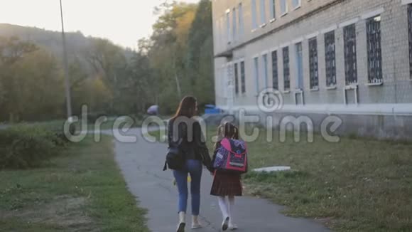 快乐的母亲带着女儿穿着校服回家妈妈和女儿正沿着学校的小巷走着视频的预览图