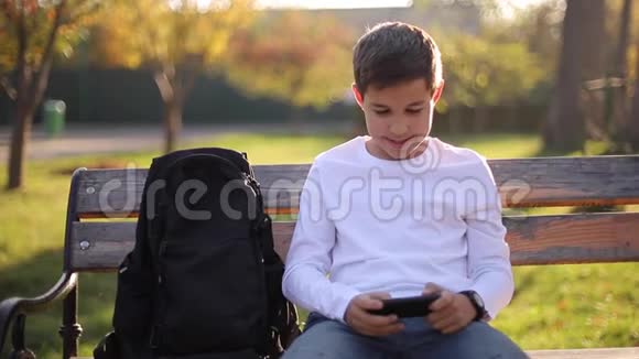 放学后十几岁的男孩在公园的智能手机上玩网络游戏视频的预览图