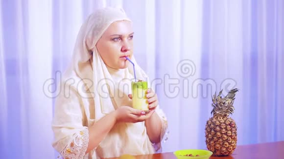 一位年轻的穆斯林妇女戴着一条浅色围巾喝着一杯水果奶昔微笑着视频的预览图