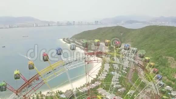 色彩缤纷的摩天轮在游乐园海上山体和现代城市景观鸟瞰设有娱乐公园视频的预览图