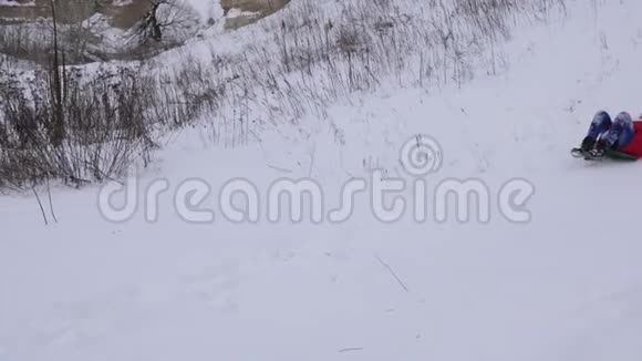 快乐的女孩从山上滑下雪孩子们在冬天的公园里滑过雪橇笑了起来慢动作视频的预览图