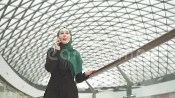 戴着头巾和背包的漂亮穆斯林女人去购物中心打电话视频的预览图