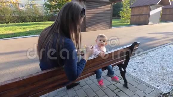 小女孩在公园里吃饭妈妈给婴儿水果妈妈和女儿坐在长凳上视频的预览图