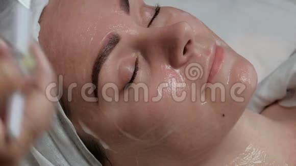 专业美容师用刷子在漂亮客户的脖子上涂上奶油一个可爱的女孩在面部护理时微笑视频的预览图