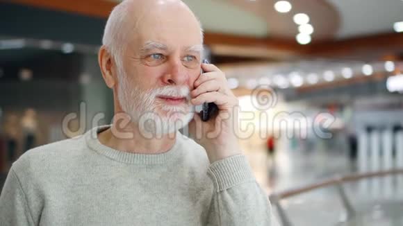 商场里穿毛衣的老人用手机购物中心的男购物者在打电话视频的预览图