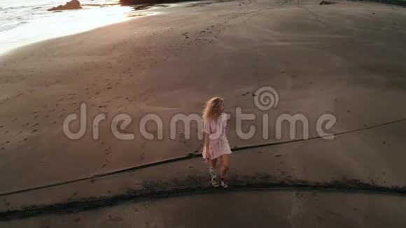 日落时在沙滩上放松的穿着帽子的快乐女孩的空中景色视频的预览图