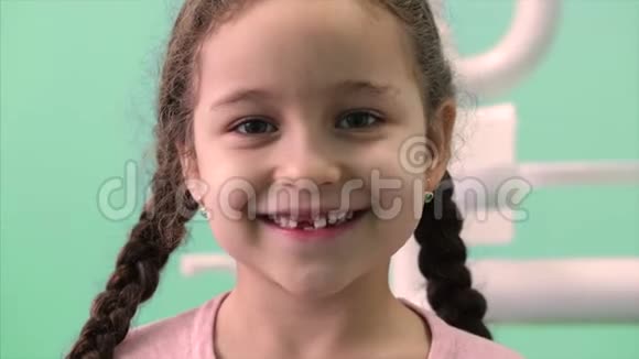 美丽的小女孩卷曲的头发和两个辫子在牙科椅微笑和看镜头显示哪里视频的预览图