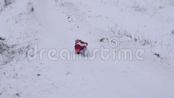 快乐的孩子在雪橇上滑雪滑梯小女孩冬天在公园里玩慢动作视频的预览图