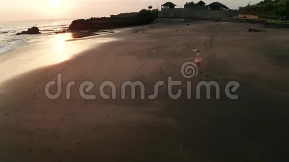 日落时在沙滩上放松的穿着帽子的快乐女孩的空中景色视频的预览图