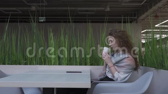 一个年轻漂亮的红头发的女人坐在咖啡馆里一边看一边拿起电话视频的预览图