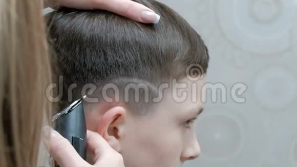 一个理发师用电裁剪器把照片剃在一个年轻人的头上的手的特写一个少年视频的预览图