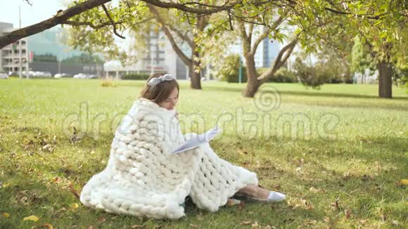 一个裹着美利奴格子的女孩在城市公园看书视频的预览图