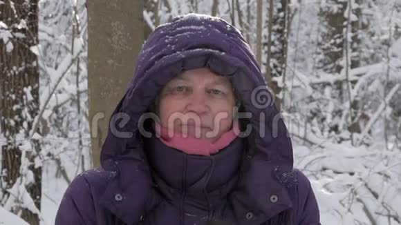 一位老妇人戴着手套拍手在冬天的森林里摇雪视频的预览图